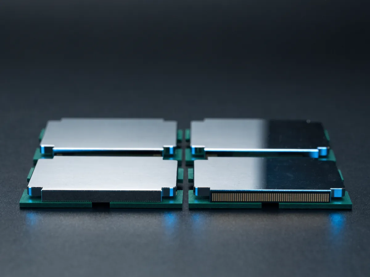 Four small square processors in a two by two grid on a dark surface, three face up and one turned over to show its contact pads
