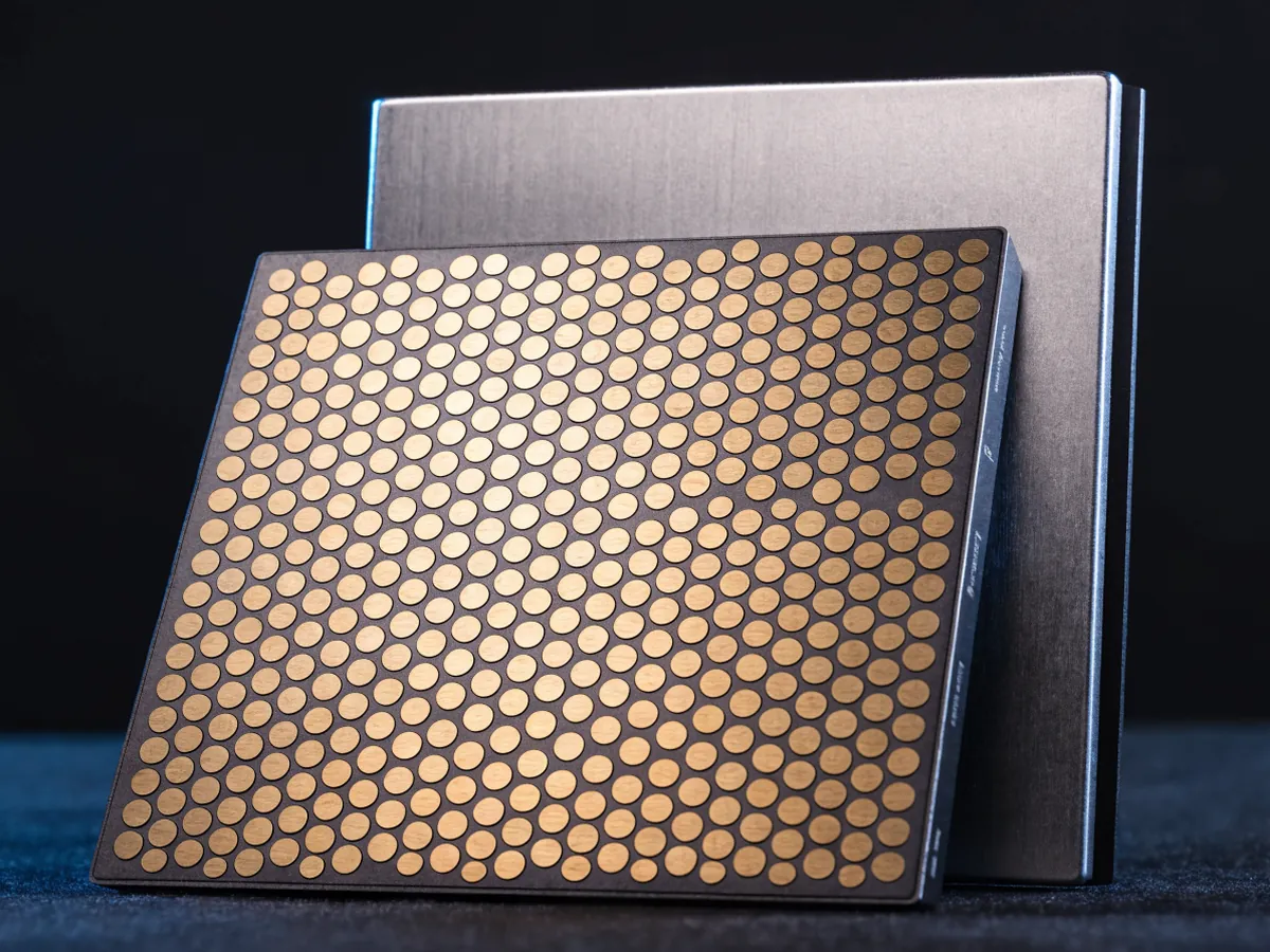 Large square processor lying face down showing its dense grid of gold contact pads, with a second standing on edge behind it