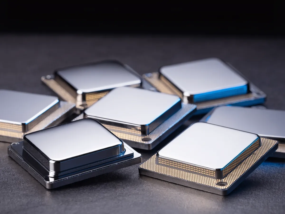 Eight small desktop processors scattered and overlapping on a dark surface, some face up with blank metal lids and some showing gold contact pads