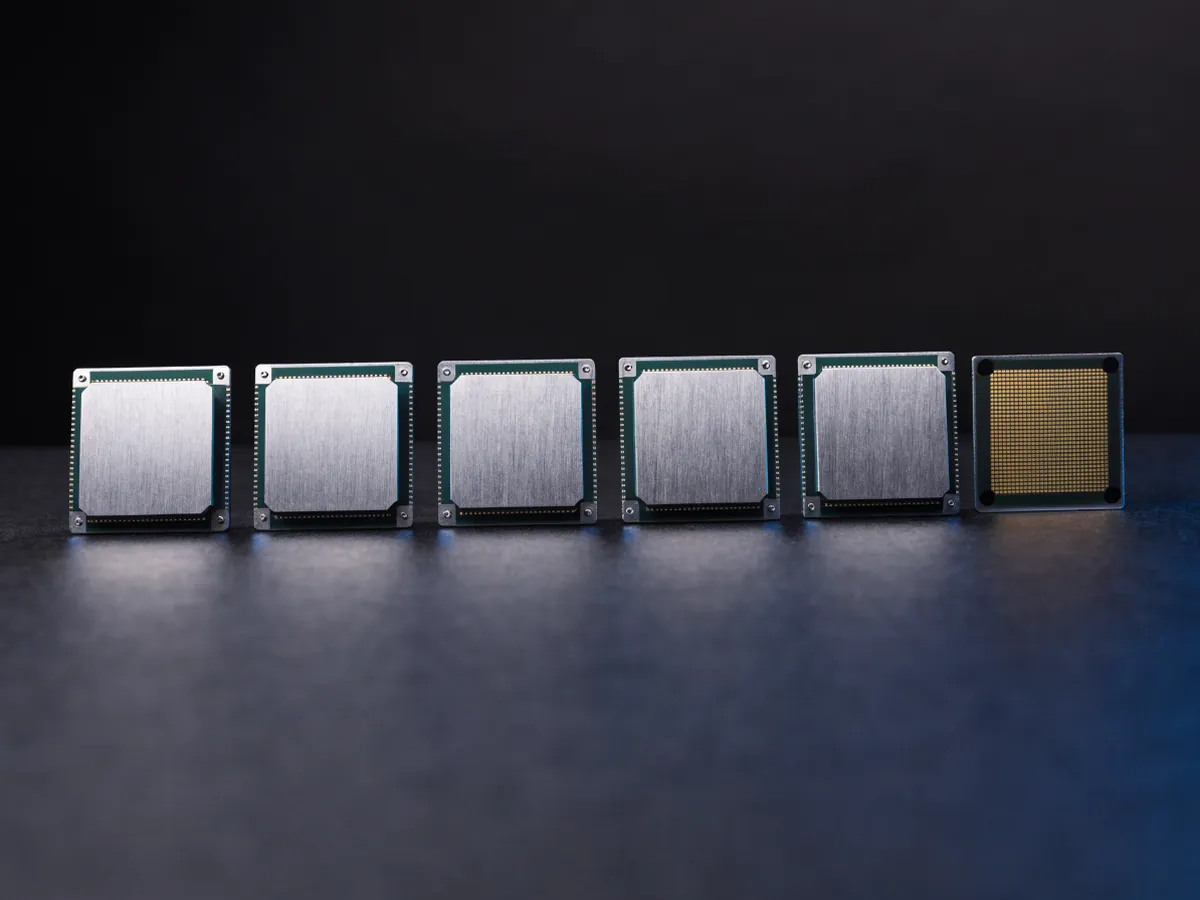 Row of five square server processors face up on a dark surface with a sixth turned over to show its gold contact pads