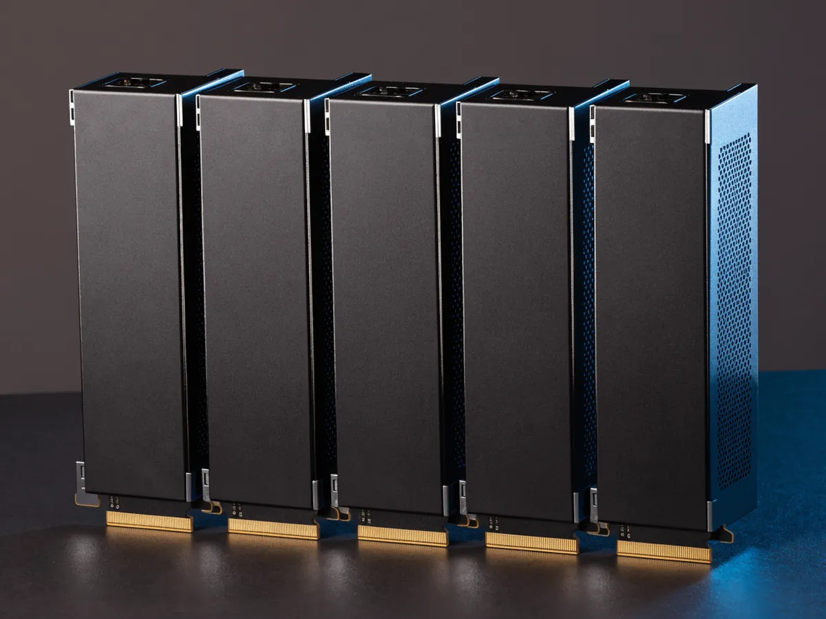 Five full length dual slot server accelerator cards standing on edge in a row, plain black shrouds with no fans and gold PCIe contacts visible, under blue studio lighting