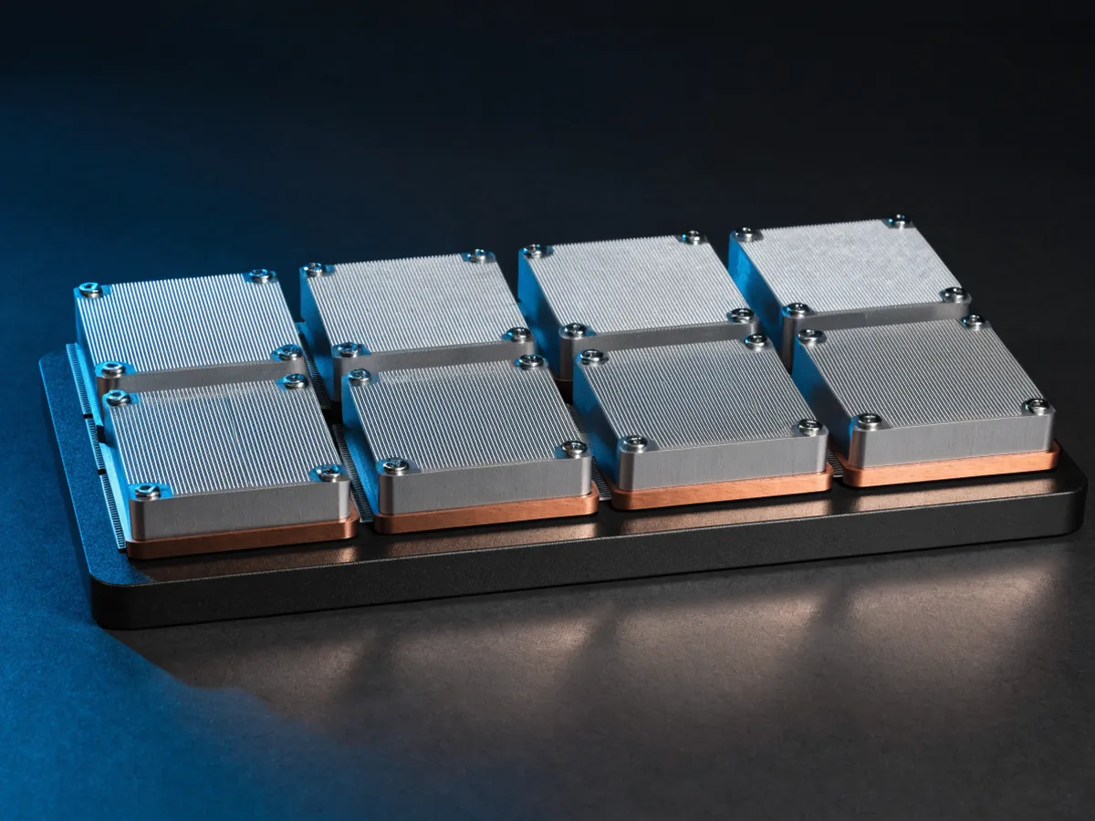 Large flat accelerator baseboard with eight square compute modules bolted on in two rows, each capped with a finned aluminium heatsink, on a dark surface