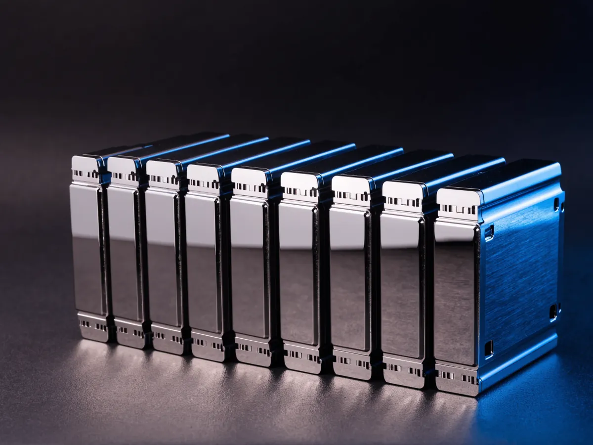 A row of eight 2.5 inch server hard drives standing on edge on a dark surface, connector edges facing the camera