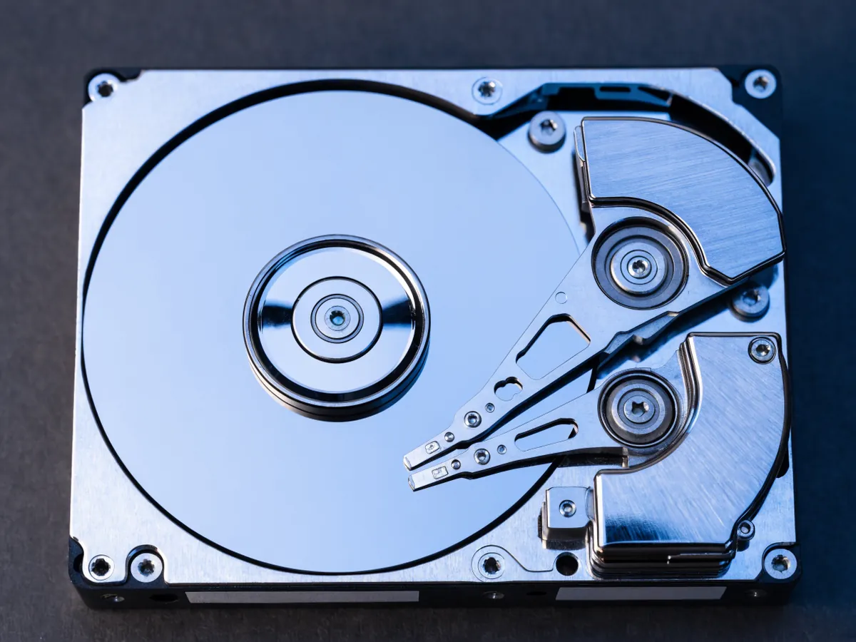 A 3.5 inch hard drive with its top cover removed, seen from above, showing mirrored platters and two stacked sets of actuator arms on one pivot
