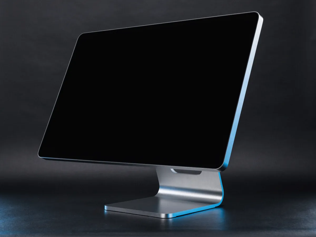 An all in one desktop computer with a blank dark screen on a hinged metal stand, photographed three quarters on a dark background