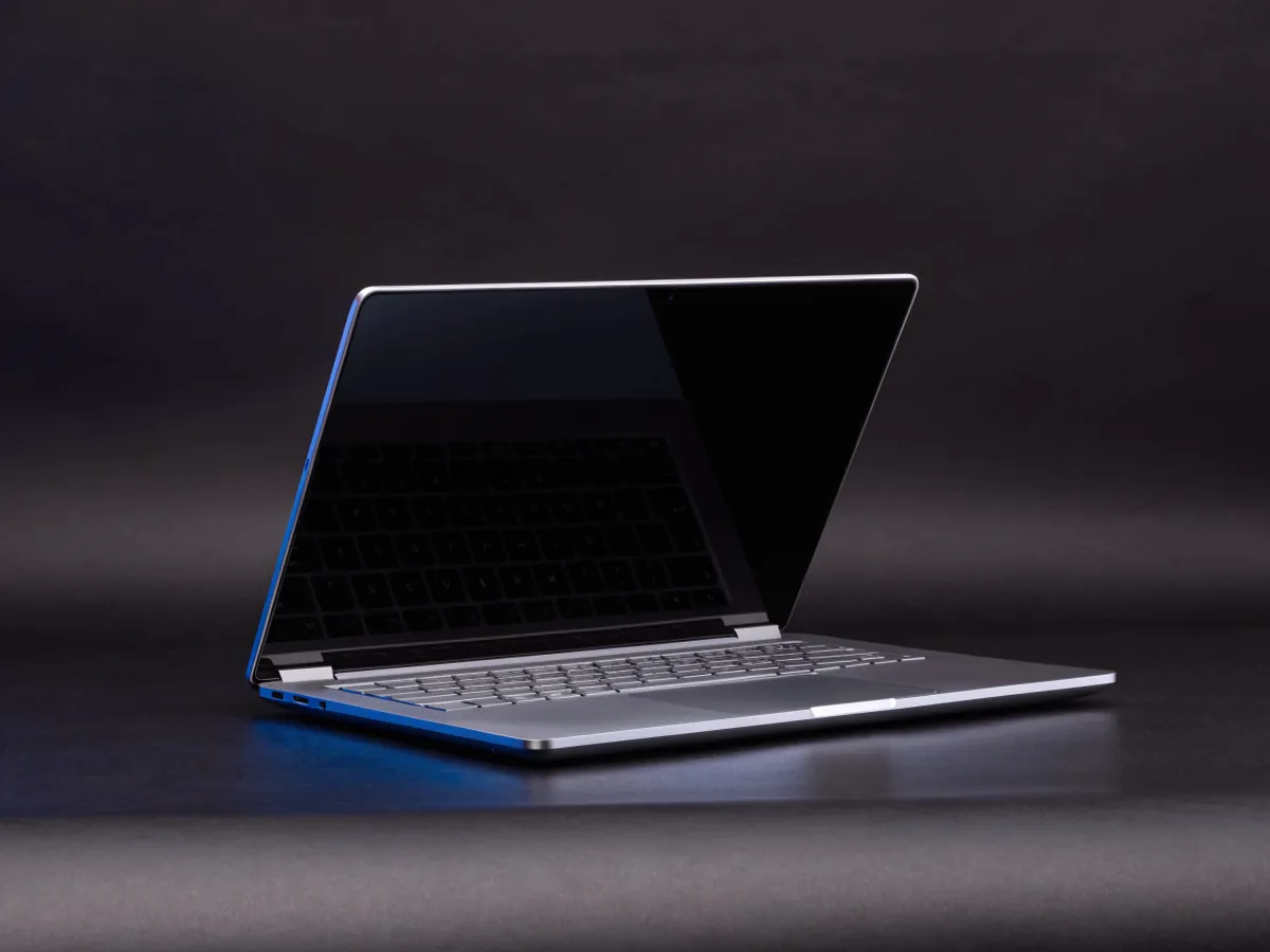 A single silver laptop open at ninety degrees with a blank dark screen and unlabelled keys, lit from behind in blue on a dark background