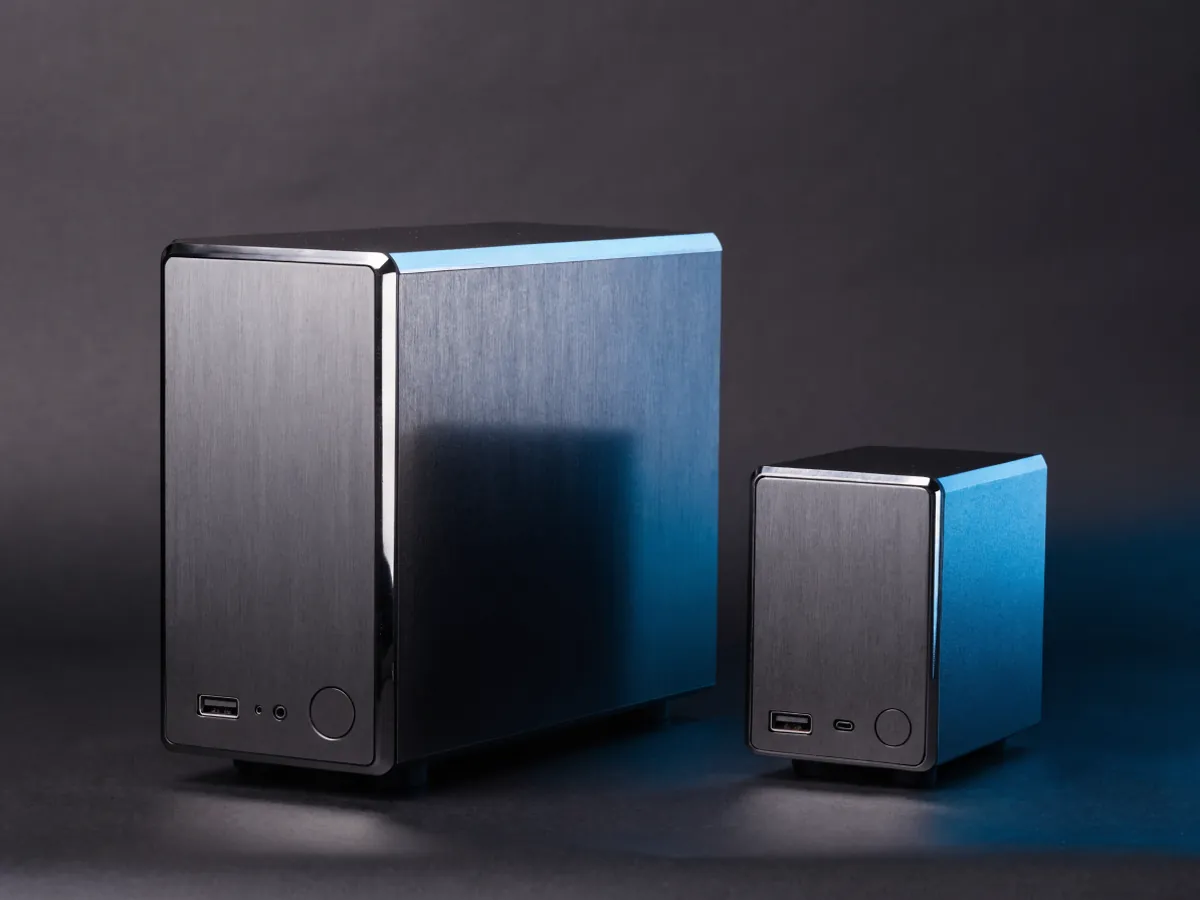A small form factor desktop chassis standing beside a much smaller one litre micro desktop, both front panels facing the camera on a dark surface