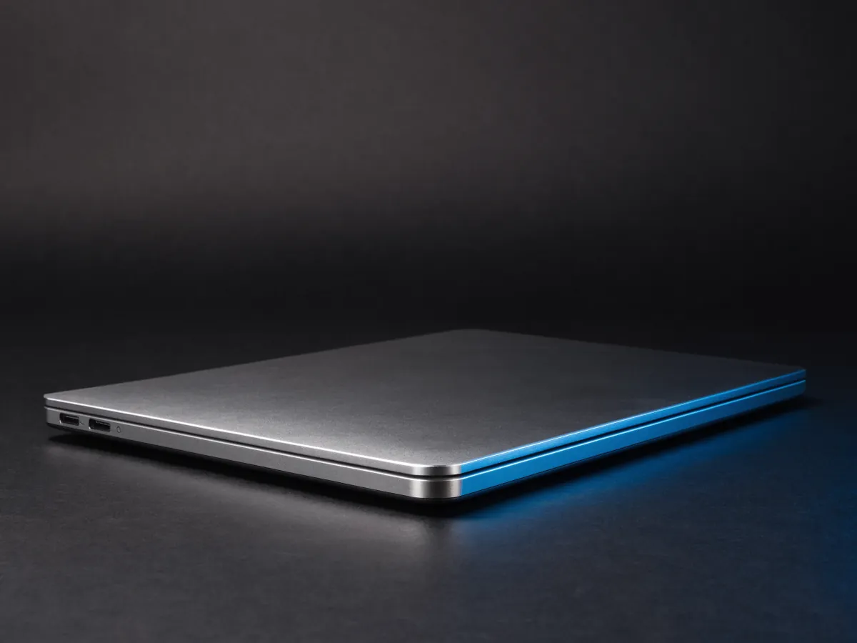 A slim closed silver aluminium notebook photographed at a low angle showing its thin edge profile and two side ports, on a dark background