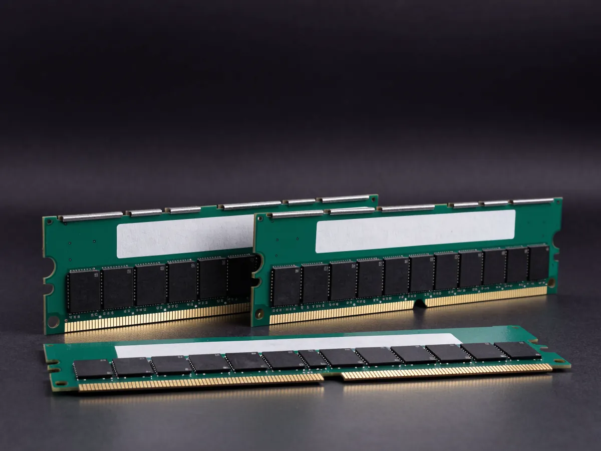 Three older generation memory modules on a dark surface, one lying flat in front with its gold contact edge and notch facing the camera