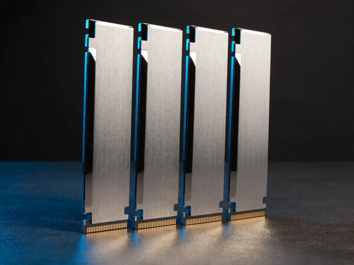 Four memory modules fitted with plain brushed aluminium heat spreaders standing upright in a row on a dark surface under blue rim lighting