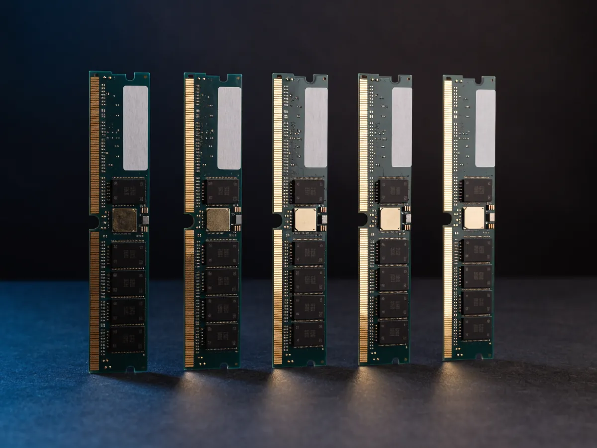 Five server memory modules standing in a row on a dark surface, each showing a larger square power management chip near the centre of the board