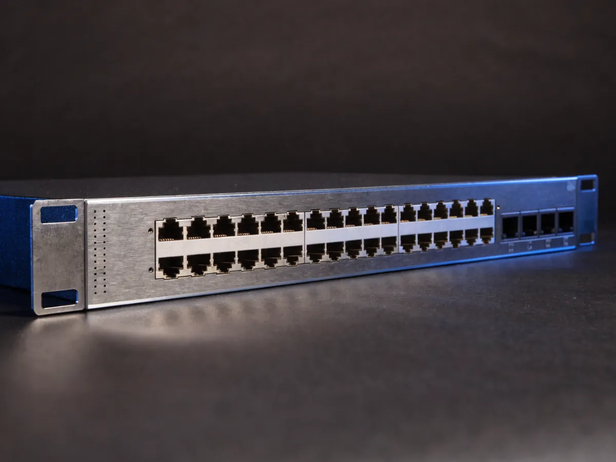 Single 1U rackmount network switch photographed at an angle on a dark background, showing a full row of forty eight copper Ethernet ports and four small uplink cages