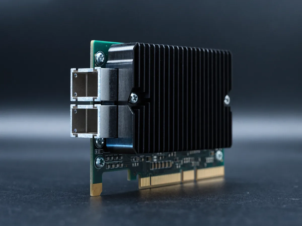 Low profile PCIe network adapter card standing at an angle on a dark background, showing a black heatsink, two square transceiver cages in the bracket and gold edge contacts