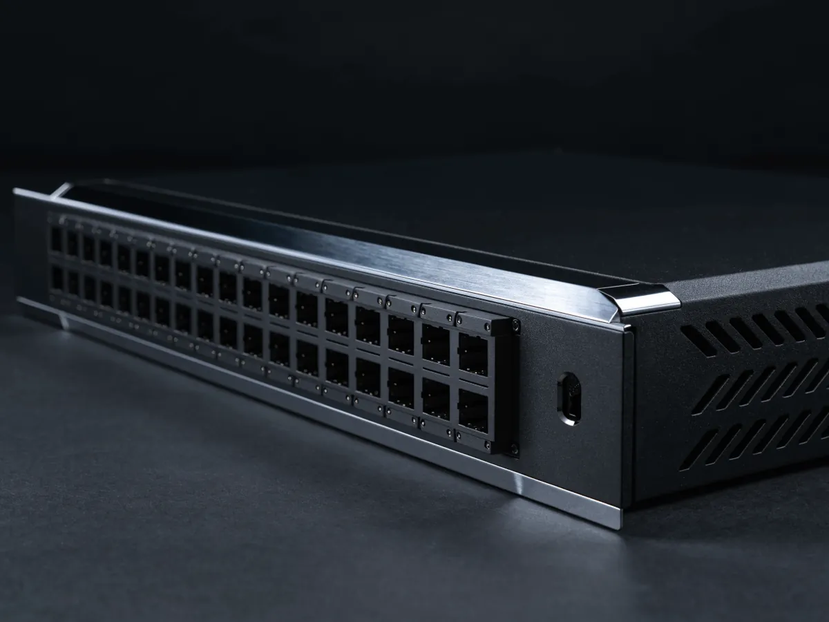 Matte black 1U rackmount switch photographed at a steep angle on a dark background, showing a dense row of thirty two large square transceiver cages and the depth of the chassis