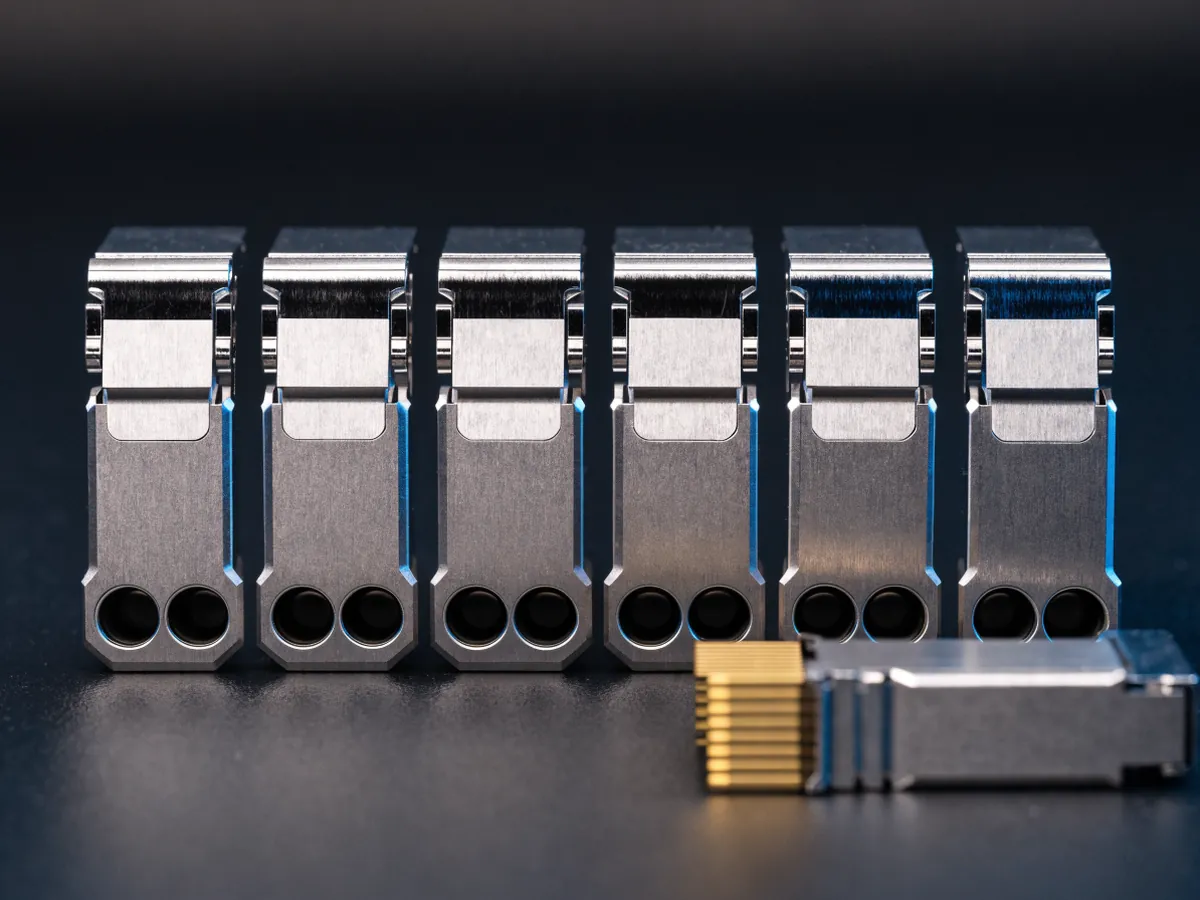 Six small pluggable optical transceiver modules on a dark background, five standing on edge showing their twin optical bores and one lying flat showing its gold contact fingers
