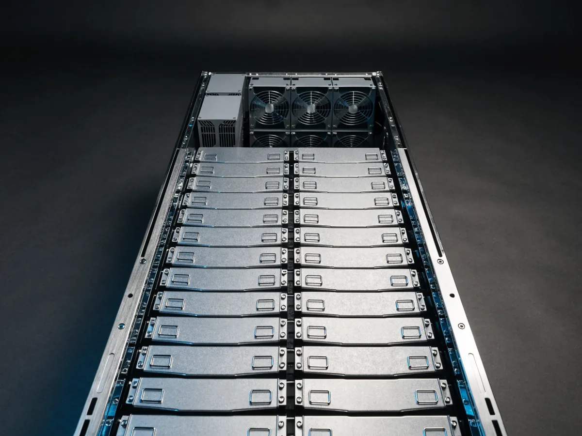 Overhead view into an open 4U storage server chassis packed with dense rows of blank 3.5 inch hard drives standing on edge in a top loading cage, under cool studio lighting