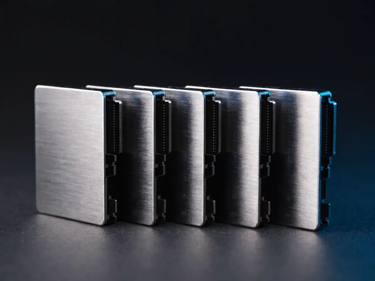 Five 2.5 inch solid state drives standing on edge in a row under cool blue studio lighting, blank metal casings with the flat connector edge facing forward